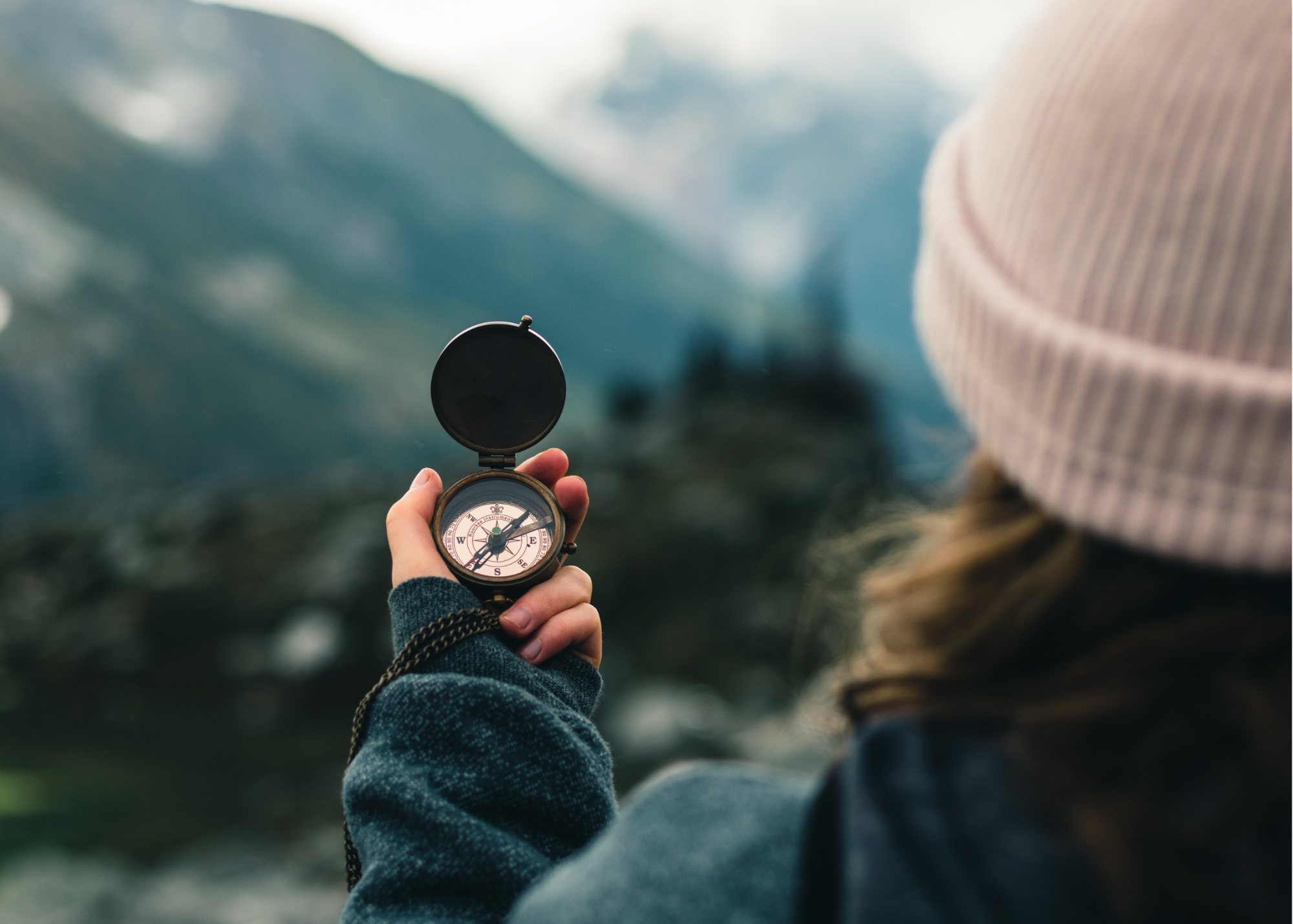 young woman traveling using compass with mountains in distance
