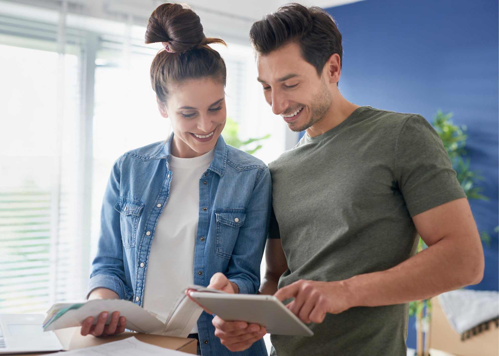 Young couple in home looking at tablet and financial paperwork