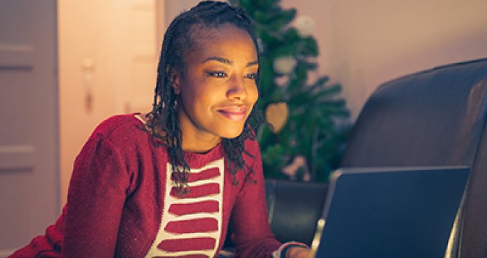Woman with holiday sweater at laptop smiling 