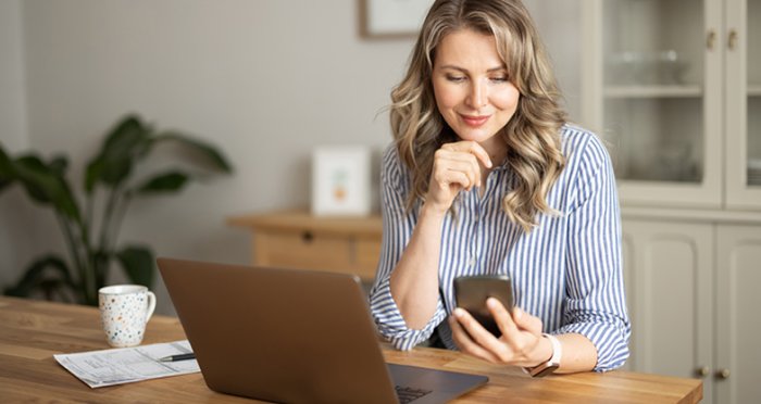 Woman tracking savings on mobile phone in kitchen and smiling