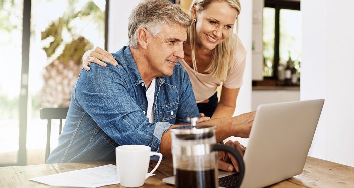 Mature couple smiling and looking at laptop computer while enjoying morning coffee