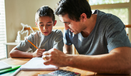 Father teaching son personal finance at table with calculator and notebook