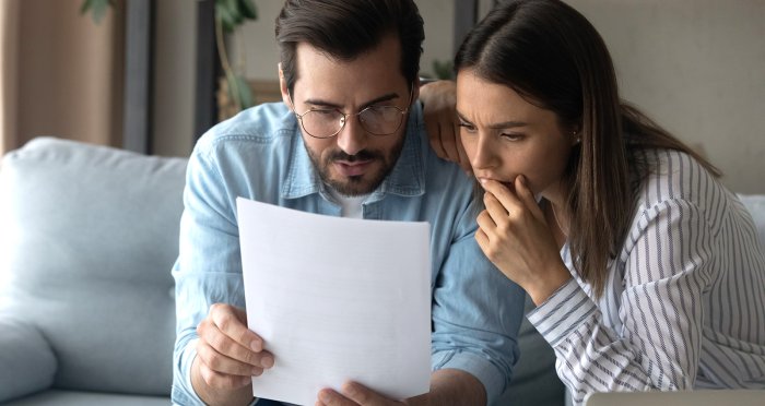 Young homeowners sitting on couch looking at letter