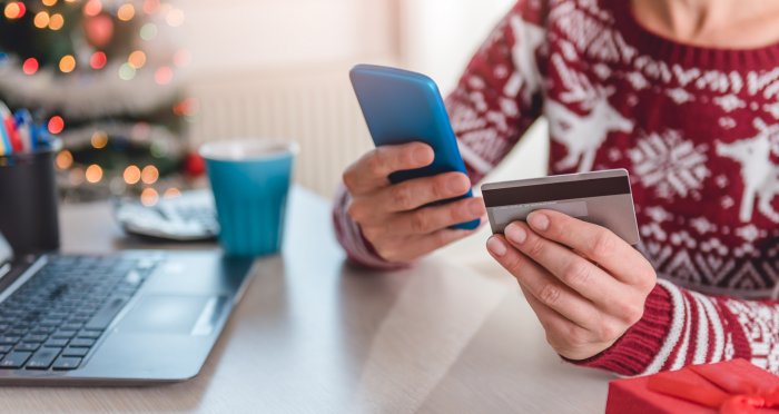 Woman in holiday sweater holding mobile phone and debit card