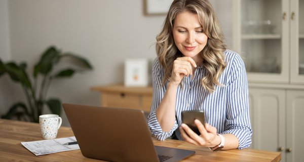 Woman tracking savings on mobile phone in kitchen and smiling